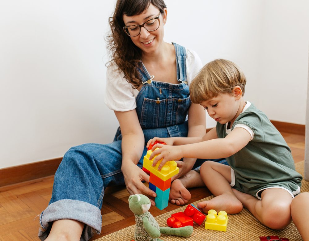 Child playing colorful blocks game with mother Cute child playing with colorful blocks with his mother sitting by. Kid playing with colorful toys with mother at home.